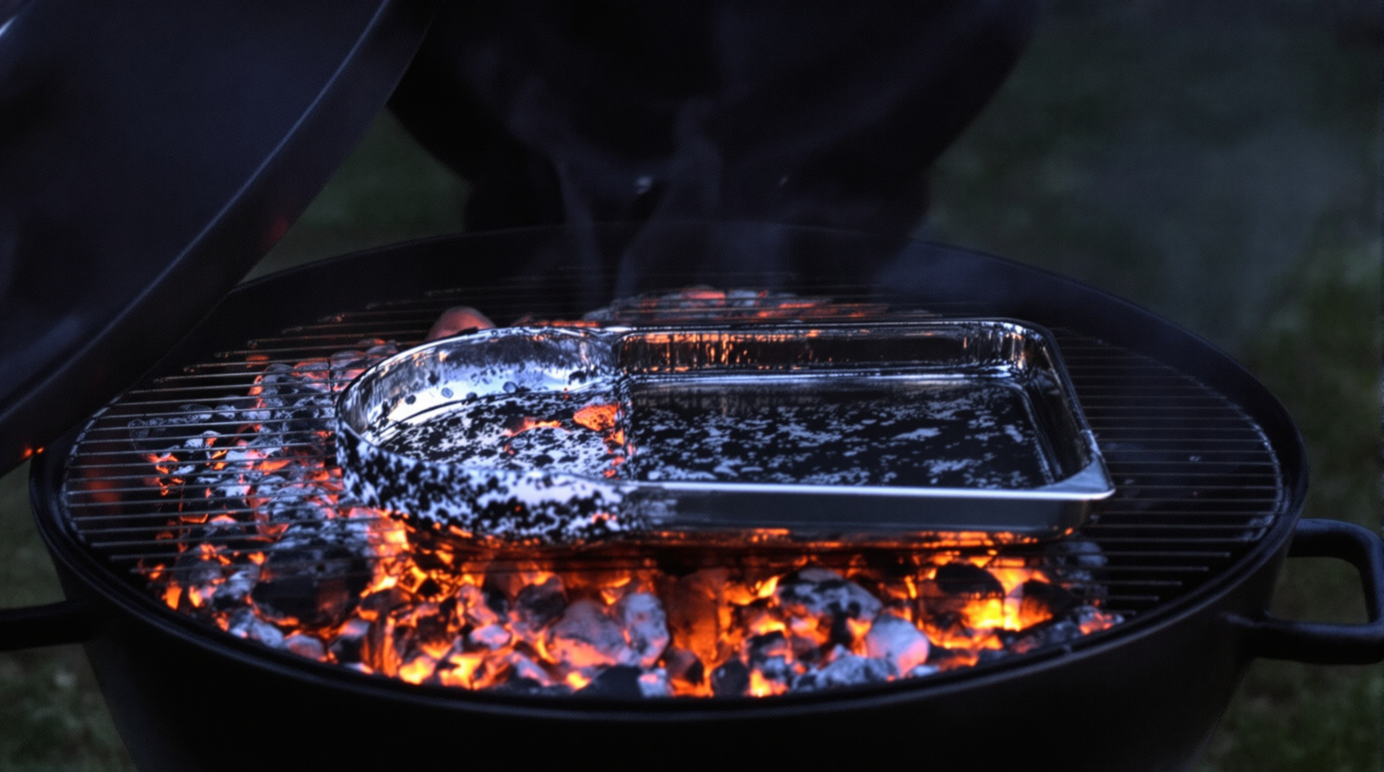Charcoal kettle grill with coals raked into two zones and a drip pan between them